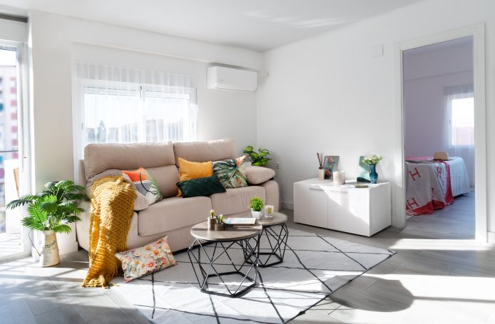 Sala de estar luminosa con sofá beige, decoración colorida y plantas.